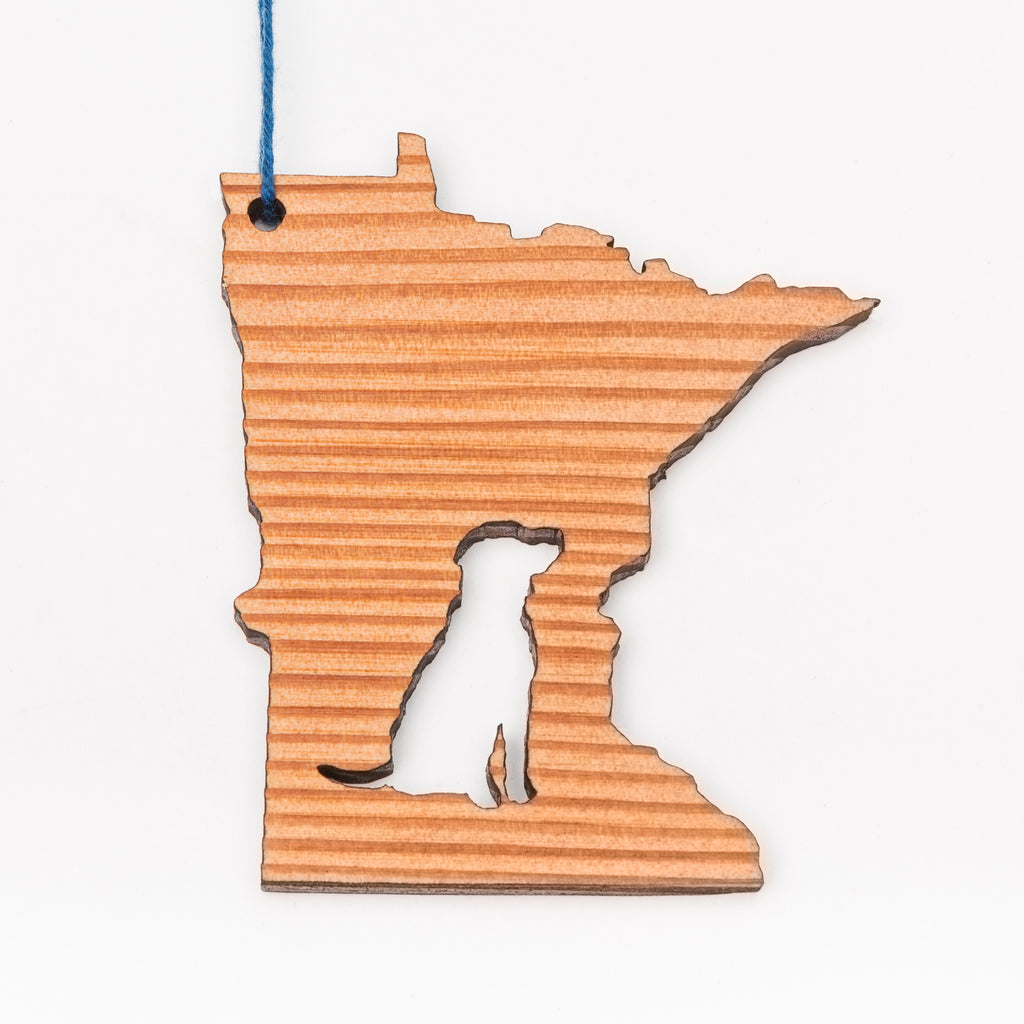 A wood ornament in the shape of Minnesota with the image of a dog cut out of the middle